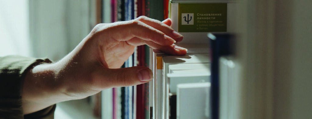 The image shows a person's hand taking a book off the bookshelf