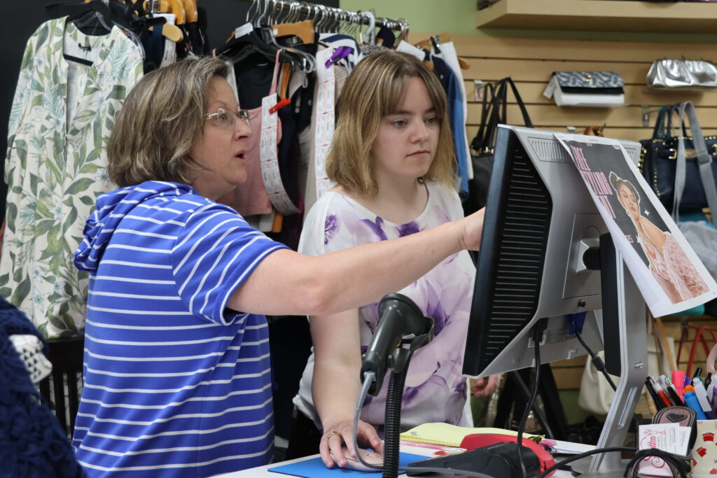 In a clothing store, a woman is pointing to the computer explaining something to the employee being trained