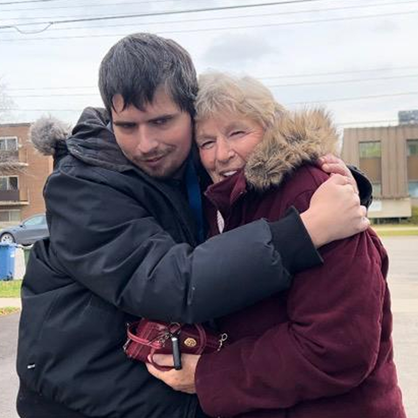 John and his mother are hugging and smiling at the camera