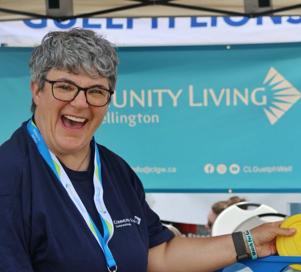 A woman is smiling and standing in front of the Community Living Guelph Wellington banner.