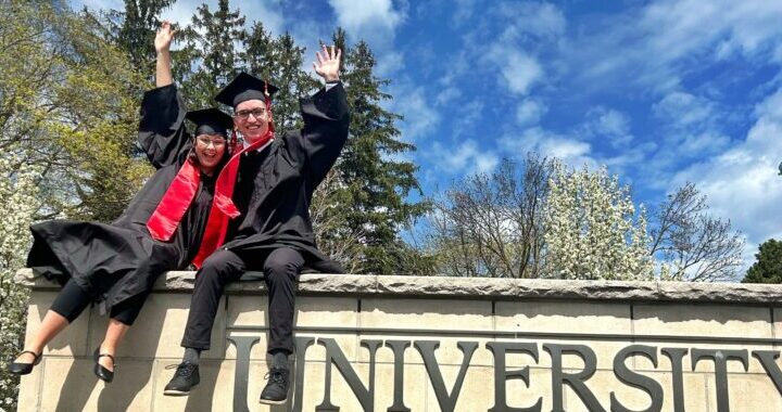Two Campus Friends graduates dressed in grad gowns and caps are sitting on top of the University of Guelph sign