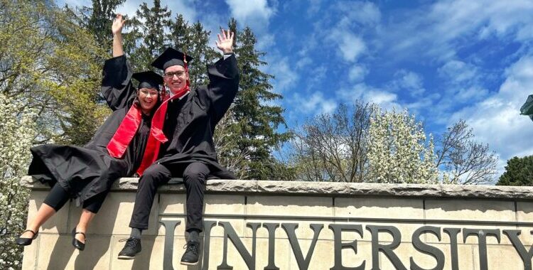 Two Campus Friends graduates dressed in grad gowns and caps are sitting on top of the University of Guelph sign